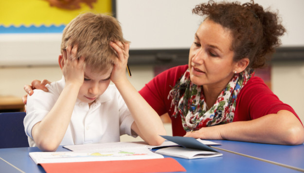 Stressed Schoolboy Studying In Classroom With Teacher